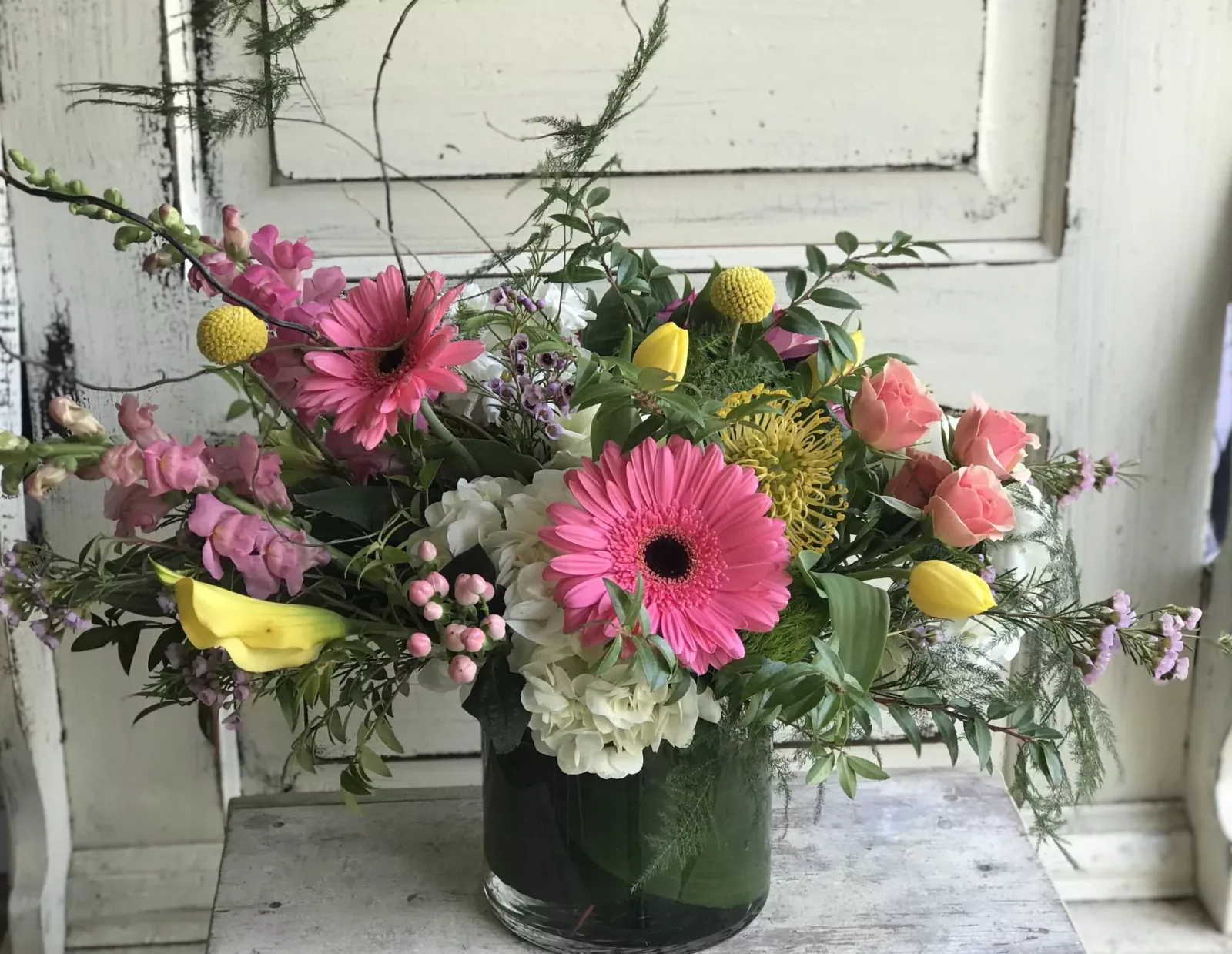 A floral arrangement in a glass bowl with gerbera daisies, mums, stock and more.