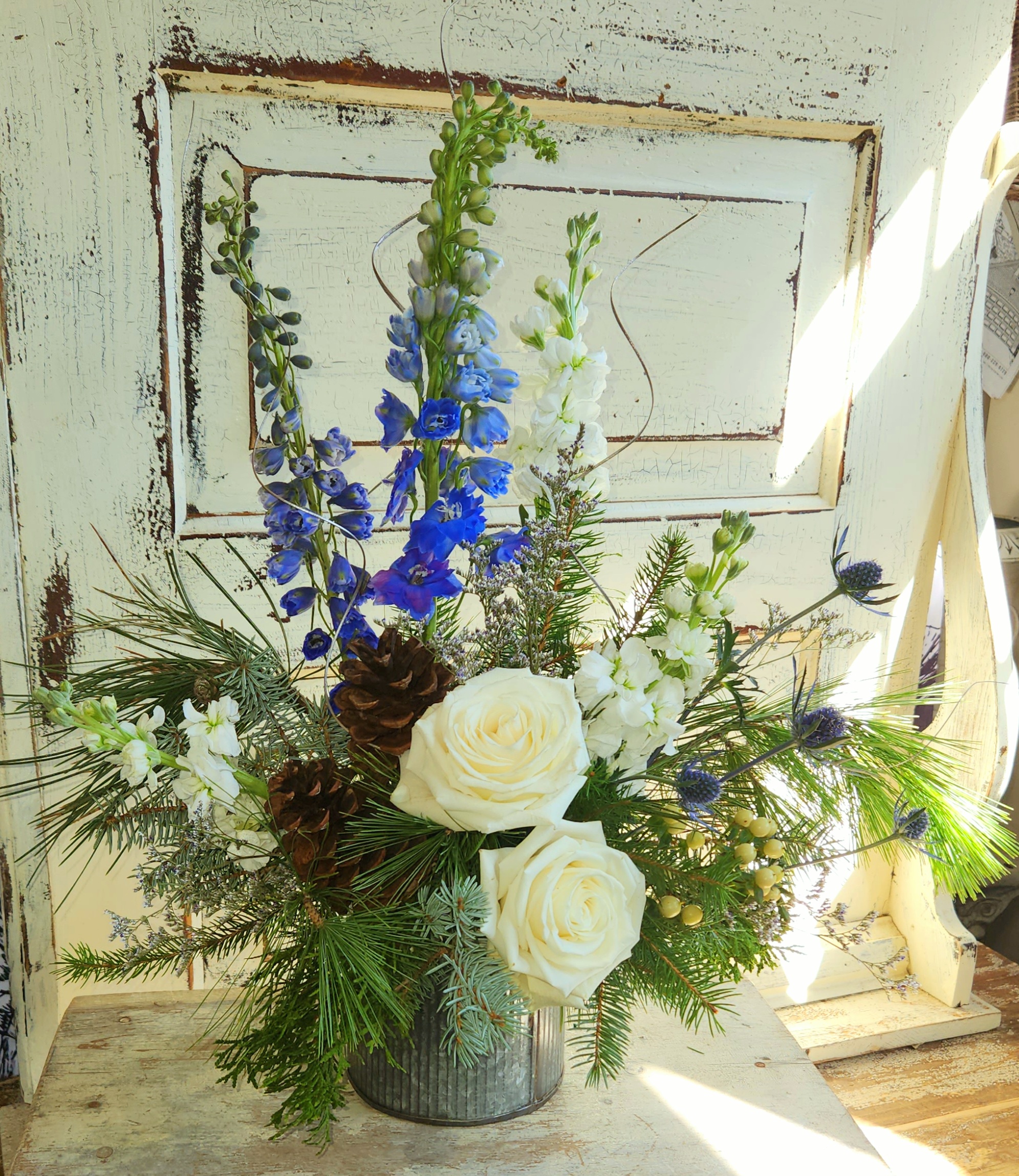 Industrial, rustic metal container with blue and white floral accents and evergreens